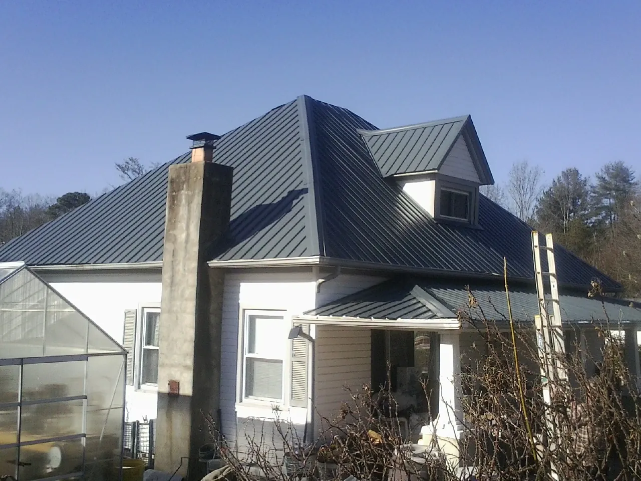 Dark blue standing seam metal roof on a white farmhouse with dormer — Slate & Tile Roof Repair by Roofing Brothers in Hildebran