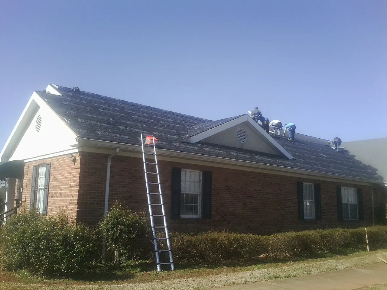 Crew tearing shingles off a brick ranch roof with a ladder set — Emergency Roof Repair work by our crew in Hildebran