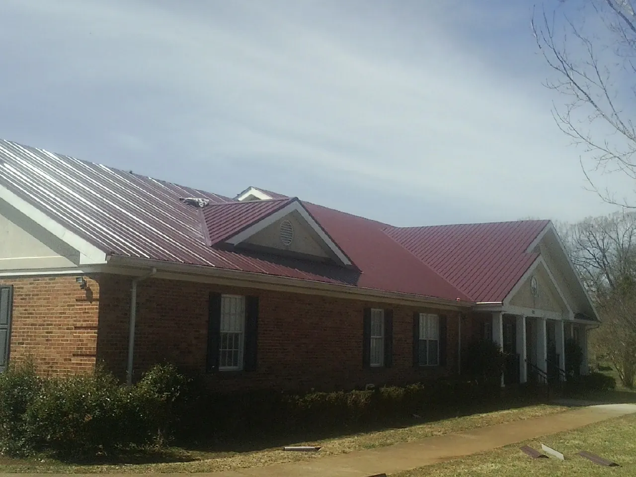 Red metal roof with gabled entries on a long brick building, from a Hail Damage Roof Repair job in Hildebran