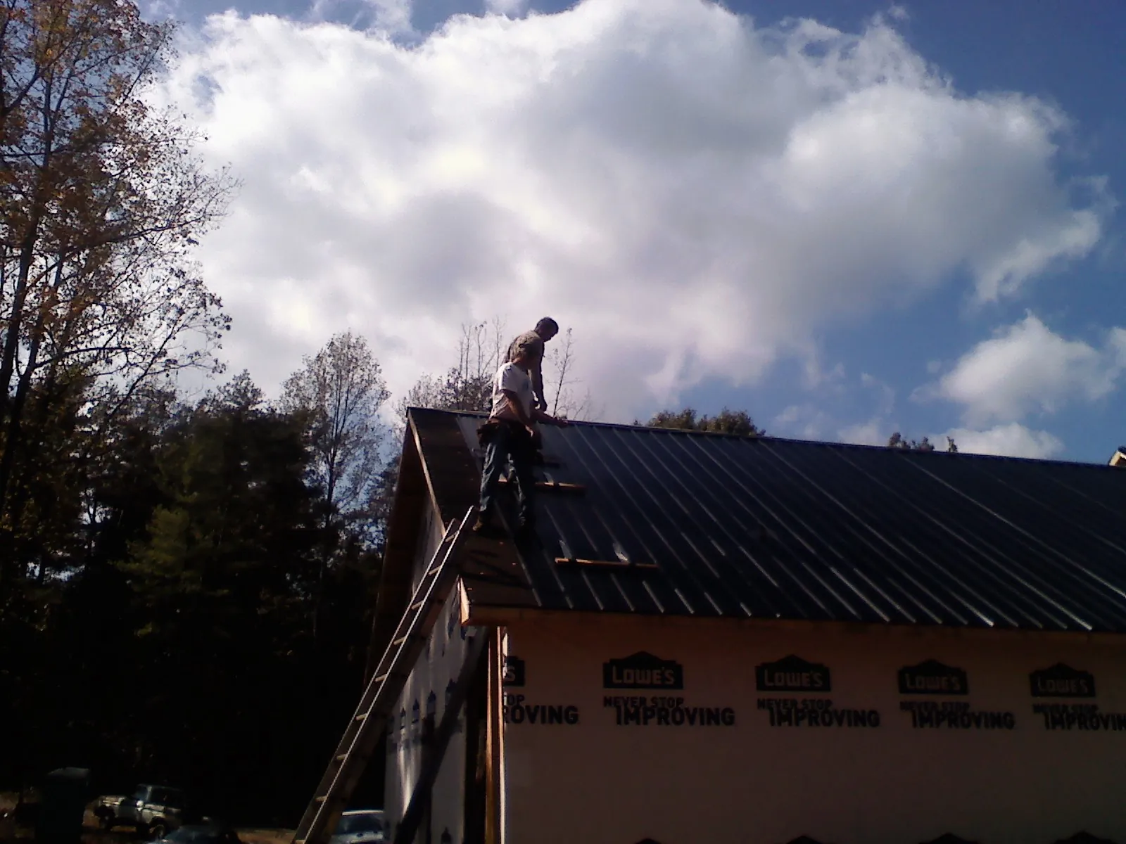 Roofer fastening dark metal panels high against a cloudy sky, from a Roof Inspection job in Hildebran