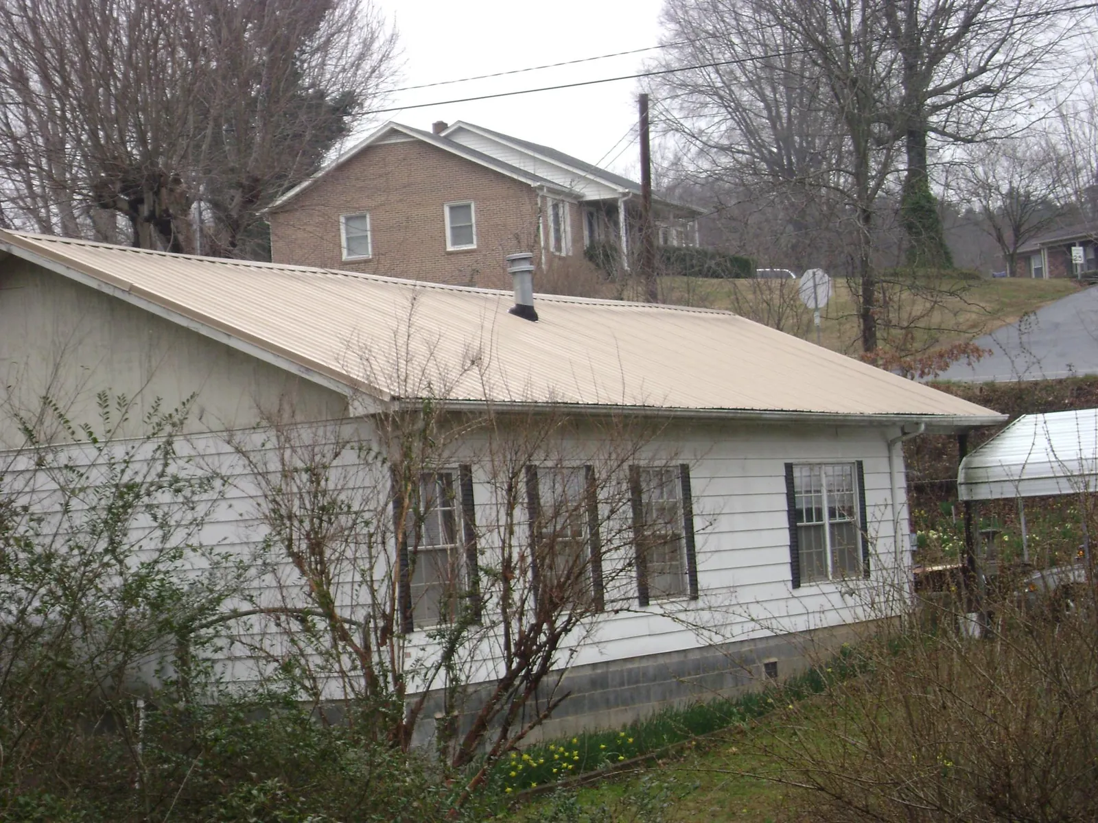 Tan metal roof on a white sided house set into a hillside — Commercial Roofing by Roofing Brothers in Hildebran